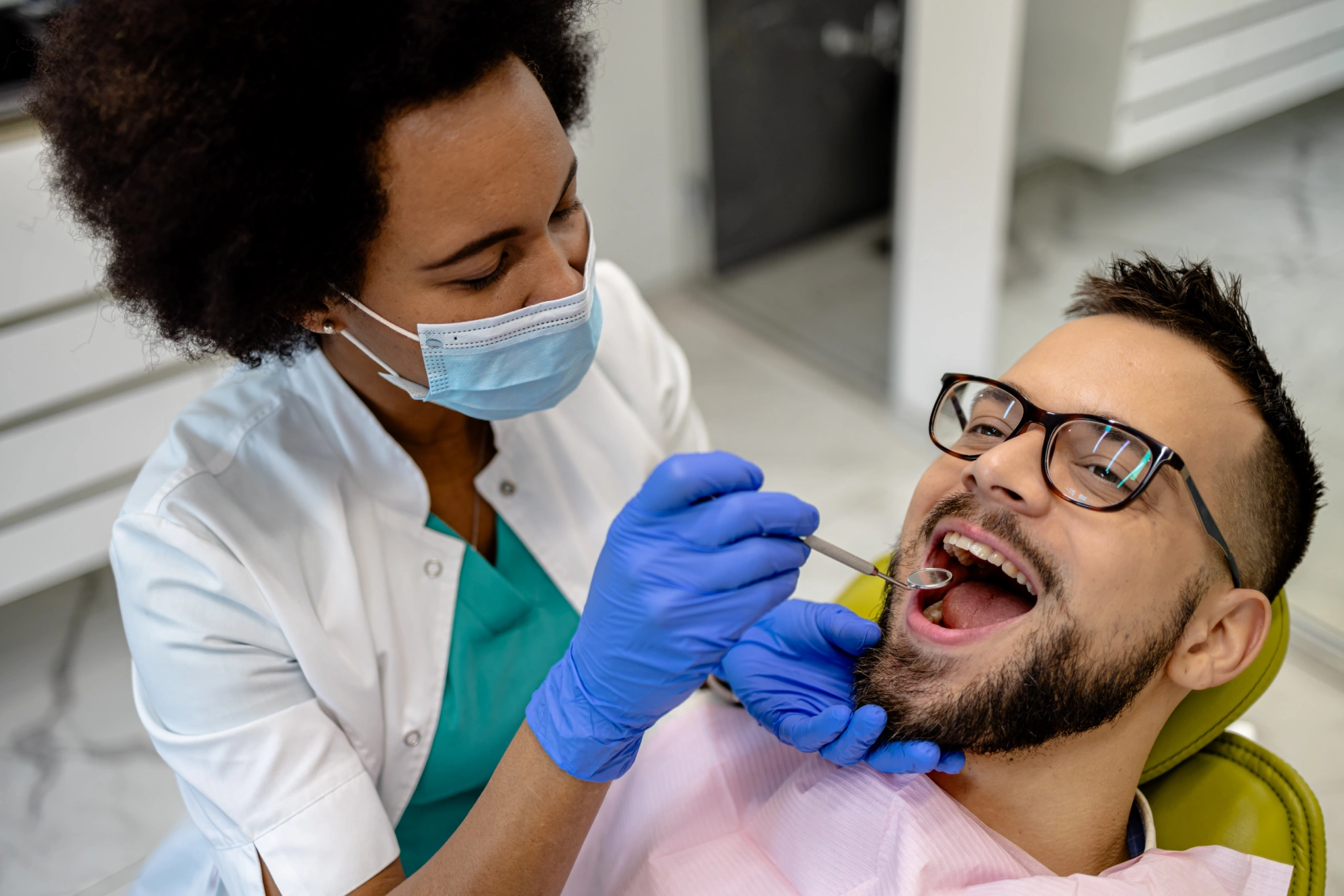 Dentist examining a patient's teeth, smiling.